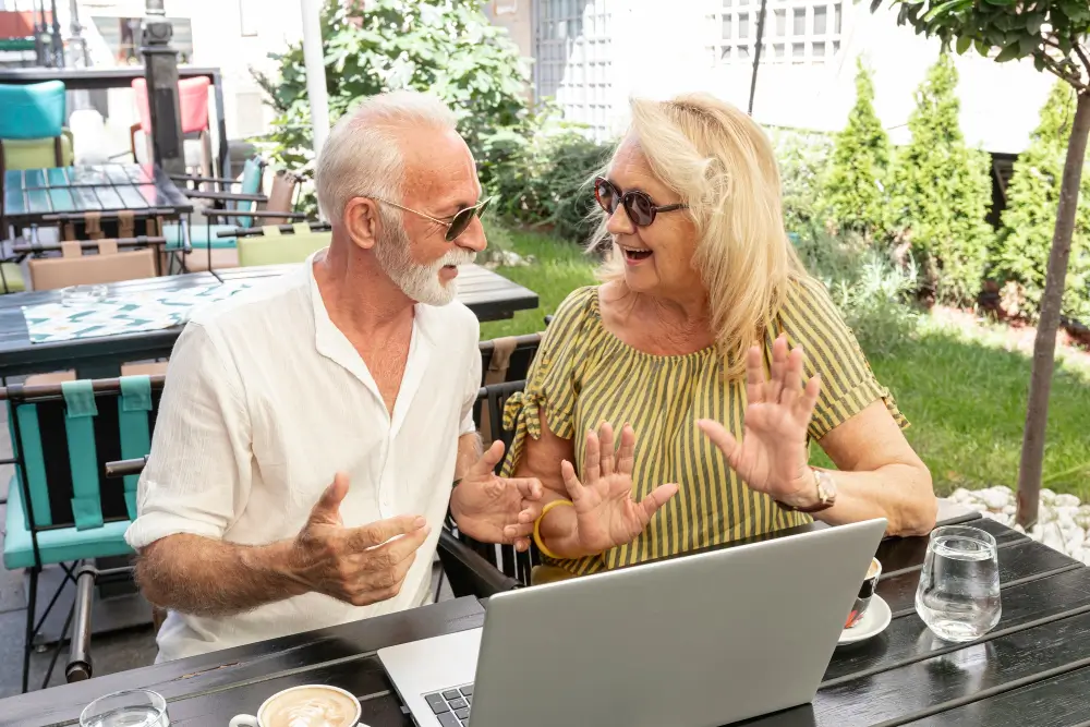 seniors over 50 on a date in a cafeteria after first meeting on a dating site. They are smiling at each others and demonstrating. There is a laptop in front of them